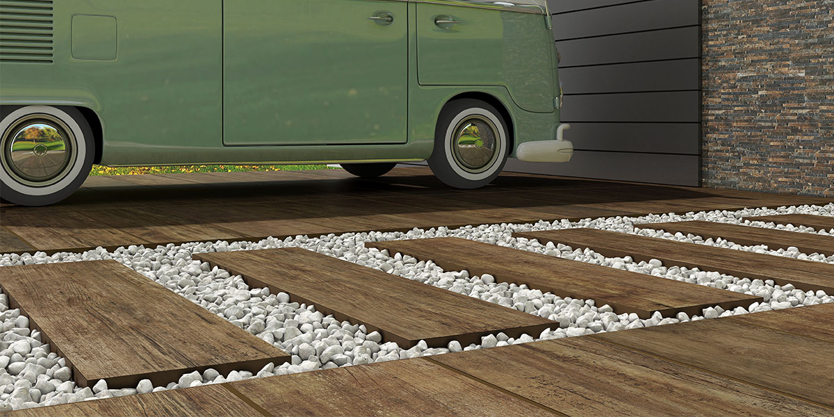 Podjazd wyłożony płytkami drewnopodobnymi ze ścieżką na podsypce, z drzwiami garażowymi i zielonym samochodem