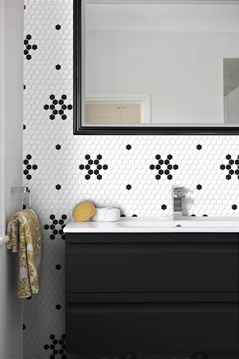 Fragment łazienki z jedną ścianą wyłożoną biało-czarną mozaiką, z czarną szafką i białym blatem, dużym lustrem i kolorowym ręcznikiem