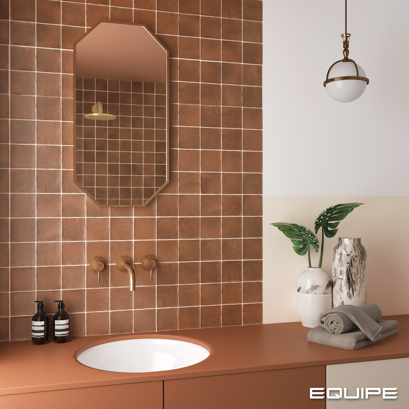 Fragment łazienki z brązowymi, kwadratowymi cegiełkami na ścianie, z brązową szafką z umywalką wpuszczaną, eleganckimi wazonami, ręcznikami i lampą wiszącą