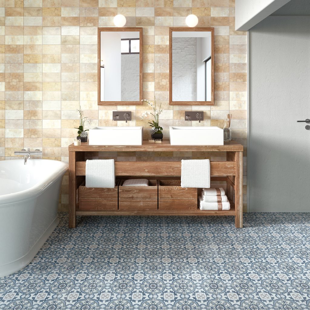 Rustykalna łazienka ze ścianą wyłożoną beżowymi cegiełkami i podłogą w niebieskie płytki patchwork Bondi Mirror Natural, z białą wanną, drewnianą szafką z dwiema umywalkami nablatowymi i dwoma lustrami z kulistymi kinkietami