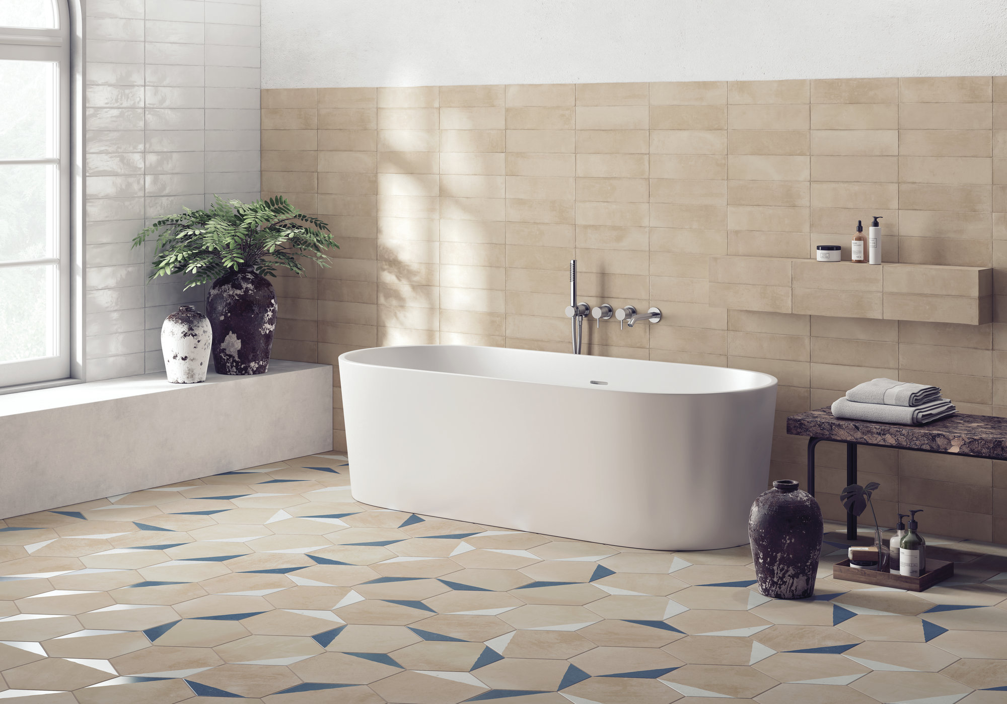 Łazienka wyłożona beżowymi płytkami heksagonalnymi z kolorowymi akcentami na podłodze oraz beżowymi i białymi cegiełkami ściennymi, z białą wanną wolnostojącą, kamiennymi dzbanami i ławą, ręcznikami i kosmetykami