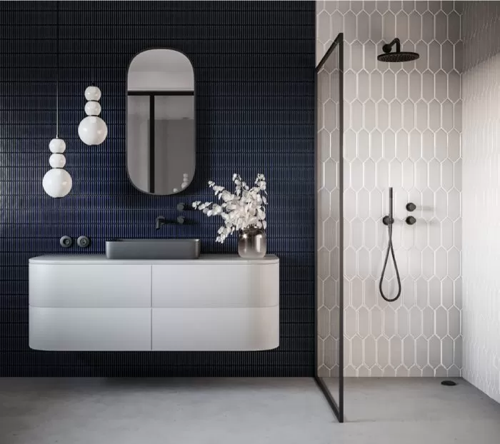 Stylowa łazienka z białą mozaiką pod prysznicem i granatową mozaiką na ścianie z umywalką, z białą szafką wiszącą i szarą umywalką, owalnym lustrem i lampą wiszącą