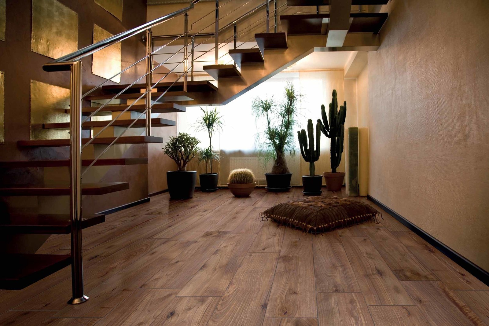 Pomieszczenie z brązowymi płytkami imitującymi drewno z poduszką, roślinami i schodami