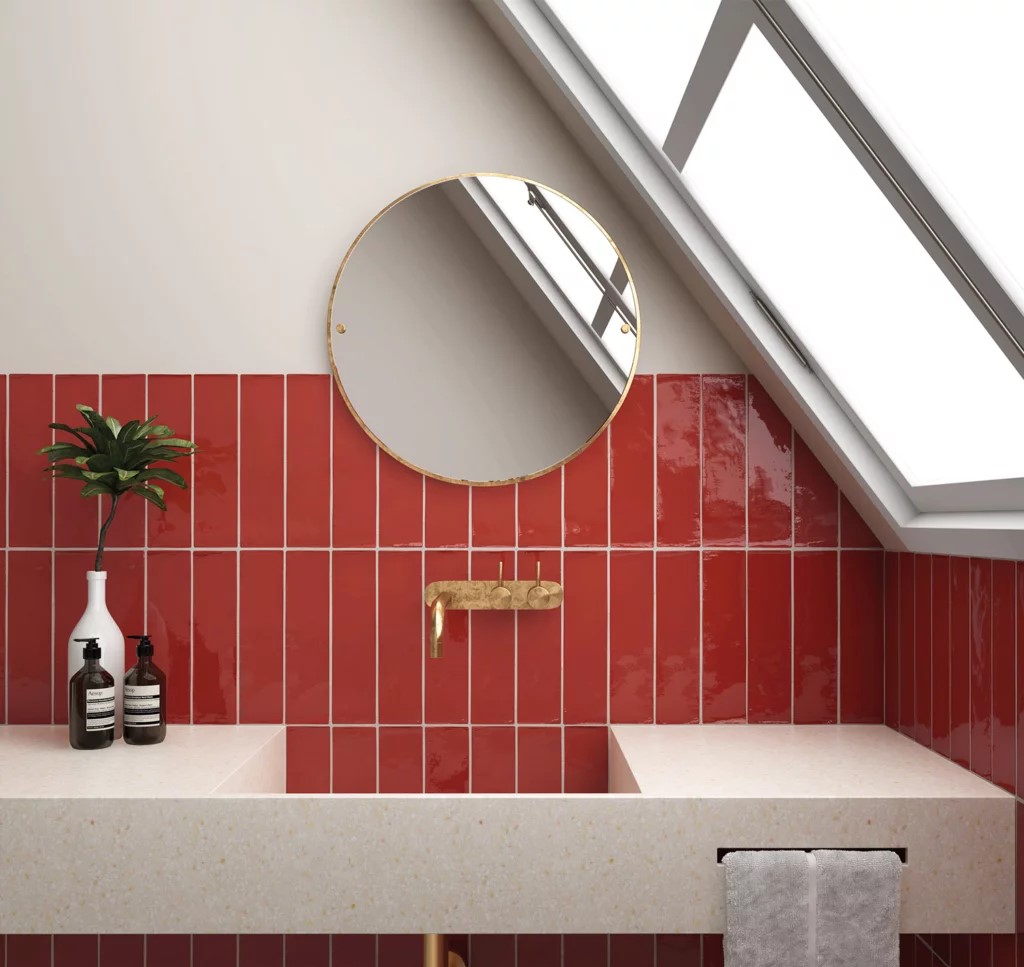Łazienka ze ścianą wyłożoną czerwonymi cegiełkami w połysku, wiszącym blatem z umywalką i okrągłym lustrem