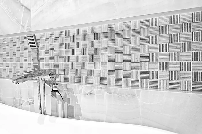 Fragment ściany w łazience wyłożony szarą mozaiką drewnopodobną oraz płytkami imitującymi kamień onyks z białą wanną oraz baterią wolnostojącą