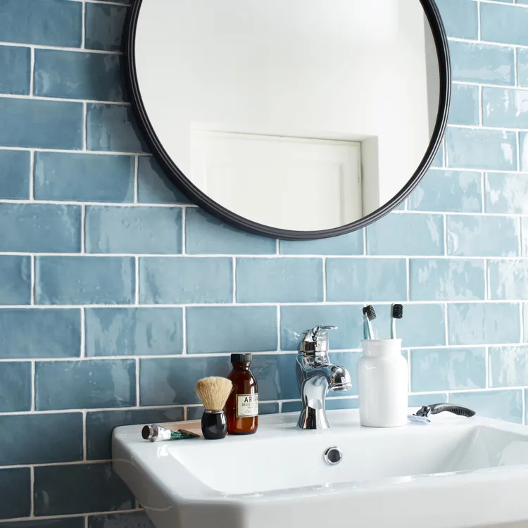 Ściana w łazience wyłożona niebieskimi cegiełkami w połysku z umywalką i okrągłym lustrem