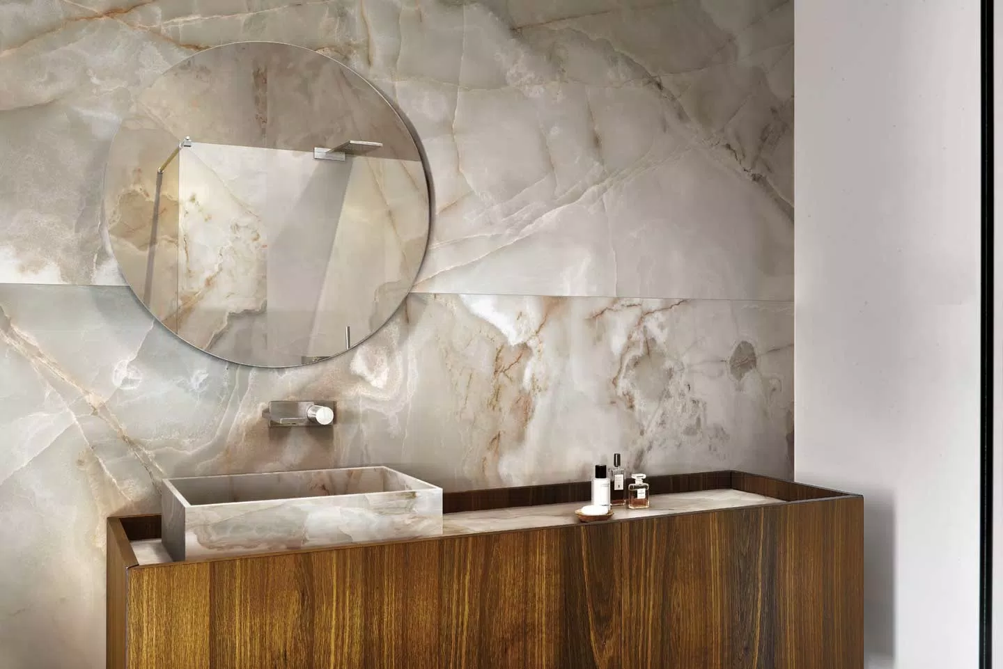 Ściana w łazience wyłożona beżowo-brązowymi płytkami imitującymi kamień onyks, z drewnianą szafką umywalką nablatową i okrągłym lustrem