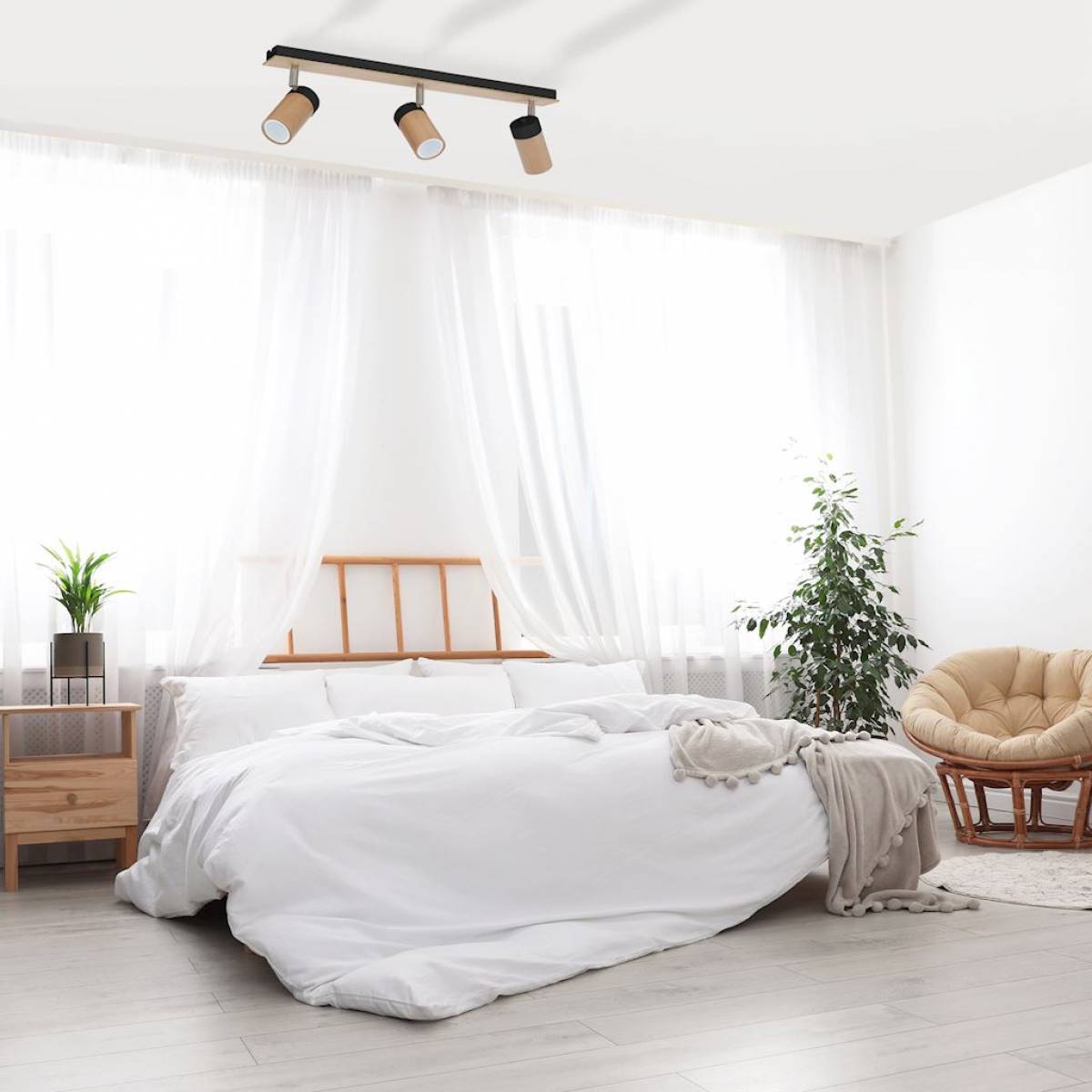 Jasna sypialnia z dużym, białym łóżkiem, fotelem, kwiatami i lampą sufitową