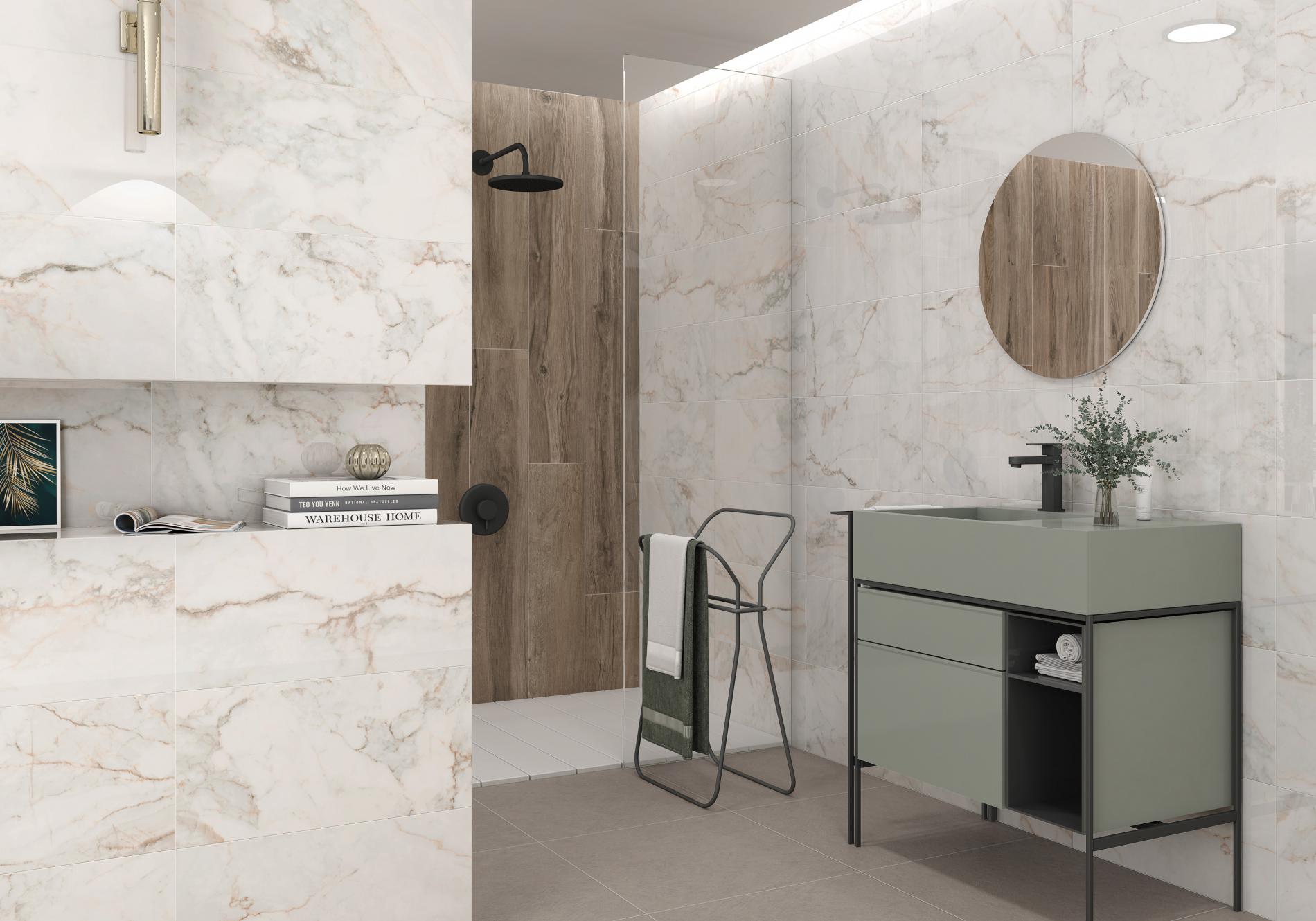 Łazienka ze ścianami wyłożonymi jasnymi płytkami imitującymi marmur i kabiną prysznicową z płytkami drewnopodobnymi, zieloną szafką z umywalką i okrągłym lustrem i wnęką w ścianie