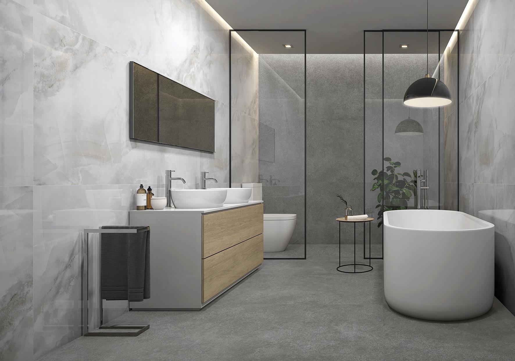 Szara łazienka wyłożona płytkami imitującymi kamień z dekoracyjną ścianą, białą wanną wolnostojącą, szafką z dwiema umywalkami nablatowymi, lustrem i szklaną ścianką, za którą jest toaleta