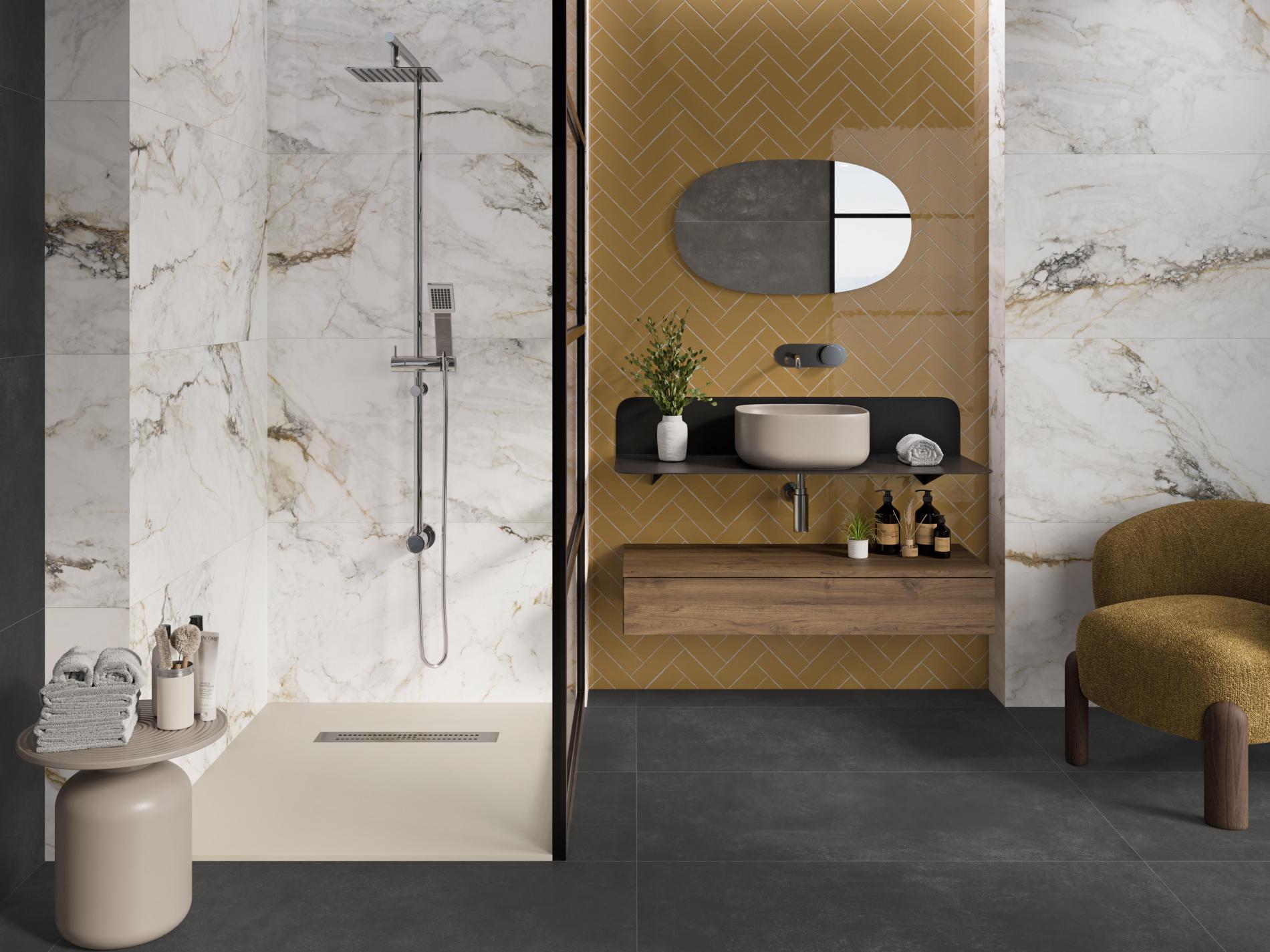 Elegancka łazienka wyłożona płytkami imitującymi marmur, beton i żółtymi cegiełkami, z dużą kabiną prysznicową, wiszącą półką z beżową umywalką nablatową, lustrem i fotelem