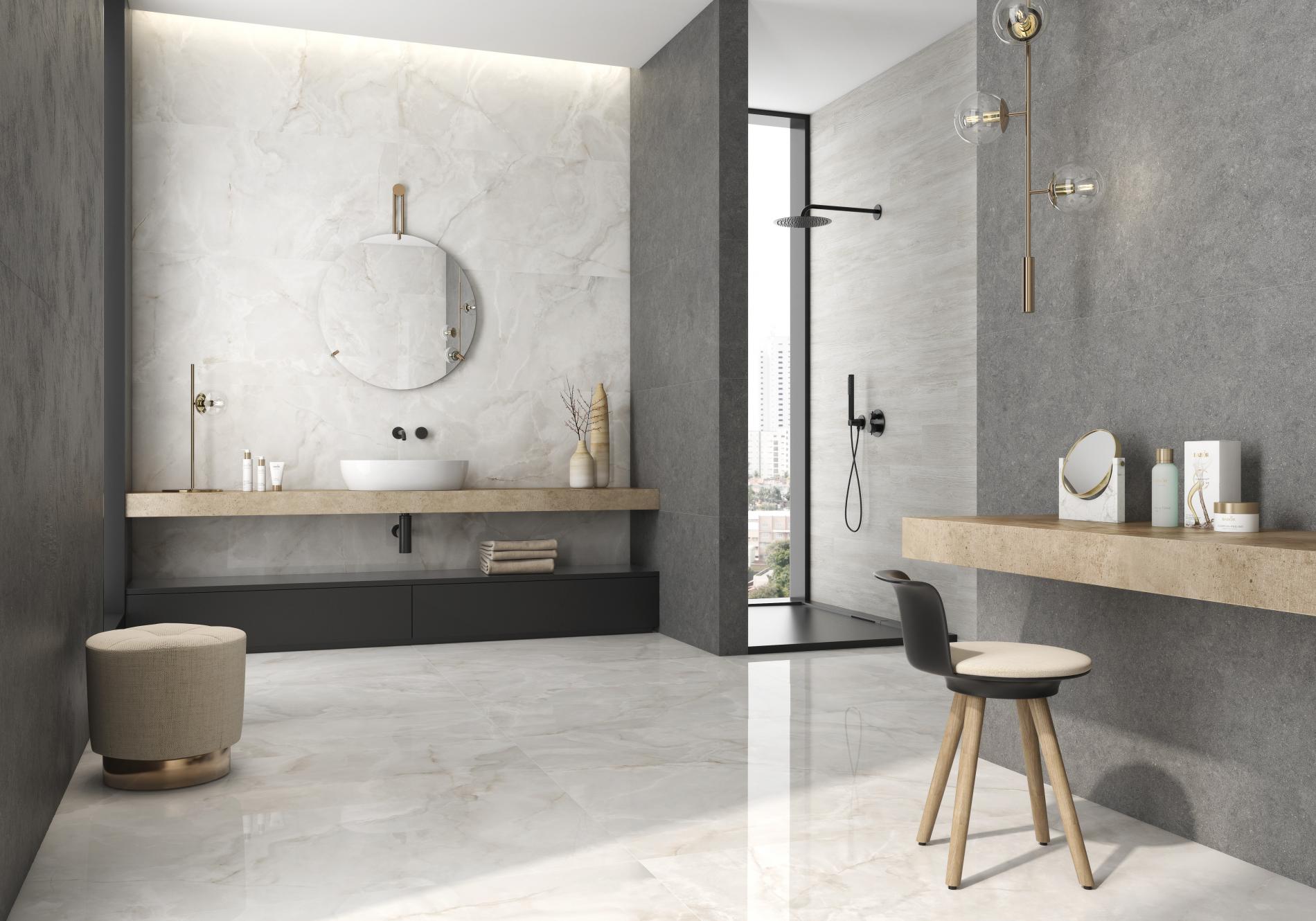 Jasna łazienka wyłożona płytkami imitującymi kamień onyks z kabiną prysznicową, wiszącą półką z umywalką nablatową z okrągłym lustrem, pufą i krzesłem