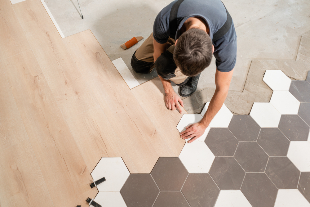 Zdjęcie przedstawiające mężczyznę przy pracy, kładącego na podłodze różne rodzaje płytek - heksagonalne i drewnopodobne