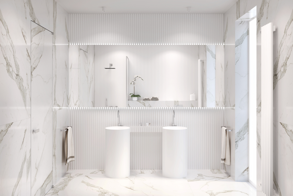 Biała łazienka wyłożona płytkami imitującymi marmur z dwiema białymi umywalkami stojącymi, dwoma ręcznikami i dużym lustrem