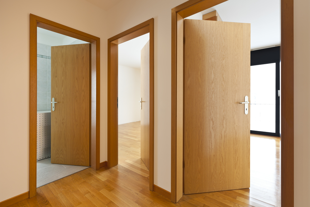 Korytarz z trzema otwartymi drzwiami, podłogą drewnopodobną i białą podłogą w łazience