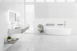 Jasna łazienka z białymi ścianami i podłogą wyłożoną jasnoszarymi płytkami imitującymi beton Shark-S Lappato, z białą wanną, półką wiszącą z dwiema umywalkami nablatowymi, lustrem i wysokim oknem