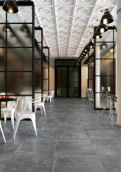 Duża restauracja z podłogą wyłożoną ciemnymi płytkami imitującymi beton Shark-N Natural z okrągłymi stolikami, białymi krzesłami, lampami wiszącymi i szklanymi przepierzeniami
