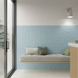 Pomieszczenie ze ścianą do połowy wyłożoną błękitnymi cegiełkami ze wzorem Casbah Decor Mix Sky Matt z wiszącą ławą z poduszkami i kinkietem