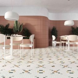 Przestronna restauracja z kolorowymi ścianami i płytkami patchworkowymi na podłodze Tesserae Play One Frutti, z okrągłymi stolikami, jasnymi krzesłami i lampami wiszącymi