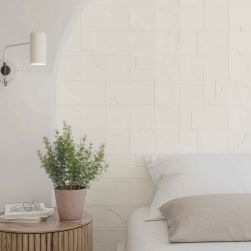 Ściana w sypialni za łóżkiem wyłożona białymi cegiełkami z reliefowanymi wzorami Casbah Decor Mix Talc Matt, z okrągłym stolikiem z kwiatem i kinkietem