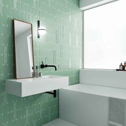Ściana w łazience wyłożona miętowymi cegiełkami Grace Sage Matt, z białą umywalką wiszącą z lustrem, kinkietem i białą wanną