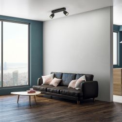 Minimalistyczny salon z dużym oknem, drewnianą podłogą, czarną kanapą skórzaną z poduszkami i niskim stoliczkiem oraz czarną lampą sufitową Porter