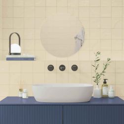 Ściana w łazience za umywalką wyłożona beżowymi cegiełkami Casbah Sand Matt, z niebieską szafką z umywalką nablatową i okrągłym lustrem