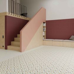 Duże, przestronne pomieszczenie z płytkami patchworkowymi Tesserae Like Grana, z kolorowymi ścianami, schodami, długą ławą z poduszkami i półkami z książkami