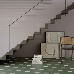 Korytarz ze ścianą wyłożoną szarymi cegiełkami 3D Stripes Grey Matt ze schodami, krzesłem, dwoma obrazami i książkami na podłodze