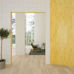 Jasne pomieszczenie z częścią ściany wyłożoną żółtymi cegiełkami w połysku Bejmat Lemonade Gloss, z fotelem, niskim stolikiem na dywanie i małym drzewkiem w donicy