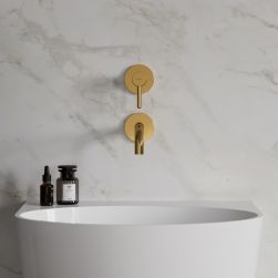 Widok od przodu na białą umywalkę ze złotą baterią podtynkową Omnires Y na tle jasnej, marmurowej ściany