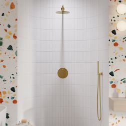 Kabina prysznicowa w półokrągłej wnęce wyłożonej białymi płytkami, a na zewnątrz płytkami lastryko ze złotym zestawem prysznicowym Y