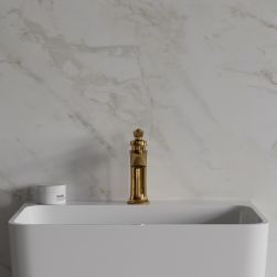 Widok od przodu na białą umywalkę ze złotą baterią stojącą Omnires Armance na tle jasnej, marmurowej ściany