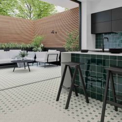 Kuchnia otwarta na taras z częścią podłogi wyłożoną białymi płytkami patchworkowymi Tesserae Suit Blanc, z zieloną wyspą, czarnymi taboretami i wiszącymi szafkami i zestawem wypoczynkowym na tarasie