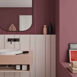 Łazienka ze ścianą wyłożoną fioletowymi płytkami PD Burgundy, z białą umywalką na różowej szafce, z lustrem i kosmetykami