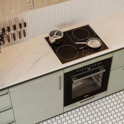 Zbliżenie na ścianę w kuchni wyłożoną białą mozaiką Miss Penny Camden z jasnymi meblami, czarną kuchenką oraz naczyniami i sztućcami