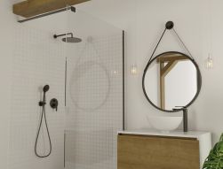 Fragment jasnej łazienki z kabiną prysznicową i czarną armaturą, białą szafką z drewnianym frontem oraz okrągłym lustrem