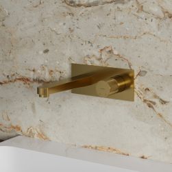Widok z boku na złotą baterię umywalkową podtynkową Omnires Contour na beżowej ścianie o kamiennej powierzchni