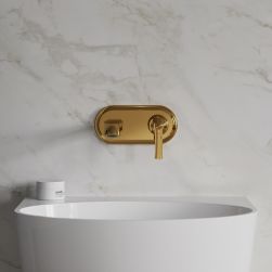 Widok od przodu na białą umywalkę ze złotą baterią podtynkową Omnires Armance na tle jasnej, marmurowej ściany