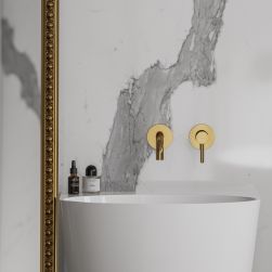 Marmurowa ściana ze złotą baterią podtynkową nad białą umywalką wolnostojącą Omnires Siena i stojącym lustrem w ramie