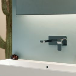Zbliżenie na baterię umywalkową podtynkową w chromie na niebieskiej ściance nad białą umywalką i pod lustrem