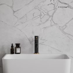 Widok od przodu na białą umywalkę z czarno-złotą baterią stojącą Omnires Y na tle jasnej, marmurowej ściany