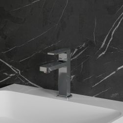Widok z boku na baterię umywalkową w chromie Omnires Baretti stojącą na białej umywalce na tle ciemnej, kamiennej ściany