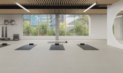 Duże, przestronne pomieszczenie z podłogą wyłożoną beżowymi płytkami imitującymi kamień Ghent Beige z ciemnymi matami do jogi i przyrządami do ćwiczeń