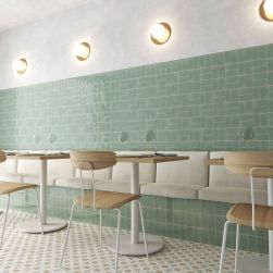 Restauracja z patchworkową podłogą i ścianą w części wyłożoną miętowymi cegiełkami w połysku Fayenza Fern Gloss, z kinkietami, poduszkami do siedzenia, stolikami i krzesłami