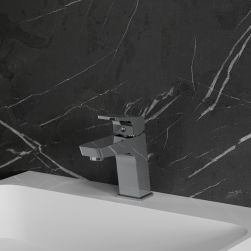 Widok z boku na baterię umywalkową w chromie Omnires Lucky stojącą na białej umywalce na tle ciemnej, kamiennej ściany