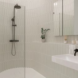 Zaokrąglona ściana w łazience pod prysznicem wyłożona jasnoszarymi cegiełkami w połysku Aquarelle O Greige z czarnym zestawem prysznicowym, białą umywalką wiszącą i lustrem