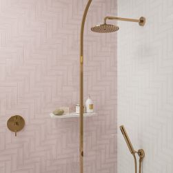 Jedna ściana pod prysznicem wyłożona różowymi cegiełkami Alchemist Primrose z drugą ścianą białą i złotym zestawem prysznicowym