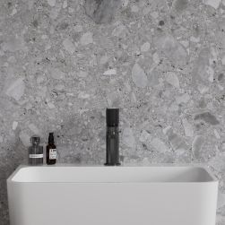 Bateria umywalkowa stojąca antracytowa Contour na białej umywalce i na tle kamiennej ściany