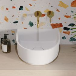Widok na białą umywalkę półokrągłą Omnires Cadence na jasnym, drewnianym blacie ze złotą baterią podtynkową na ścianie lastryko